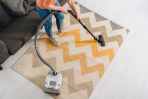 Cropped view of woman cleaning carpet with vacuum cleaner