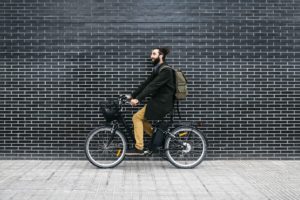 Man riding e-bike along a brick wall
